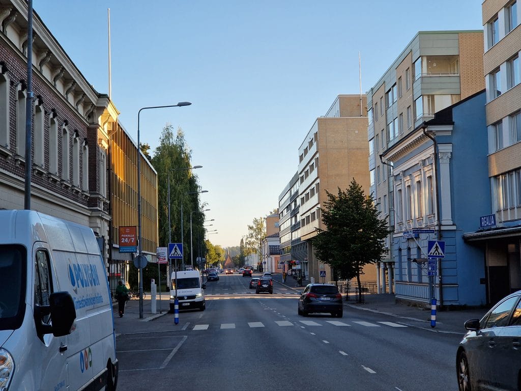 Kaupunkimaisema 2020-luvulla Mikkelissä. Asfaltoidun kadun molemmin puolin kerrostaloja. Autoja liikenteessä, osa pysäköitynä. Muutama ihminen jalkakäytävällä.