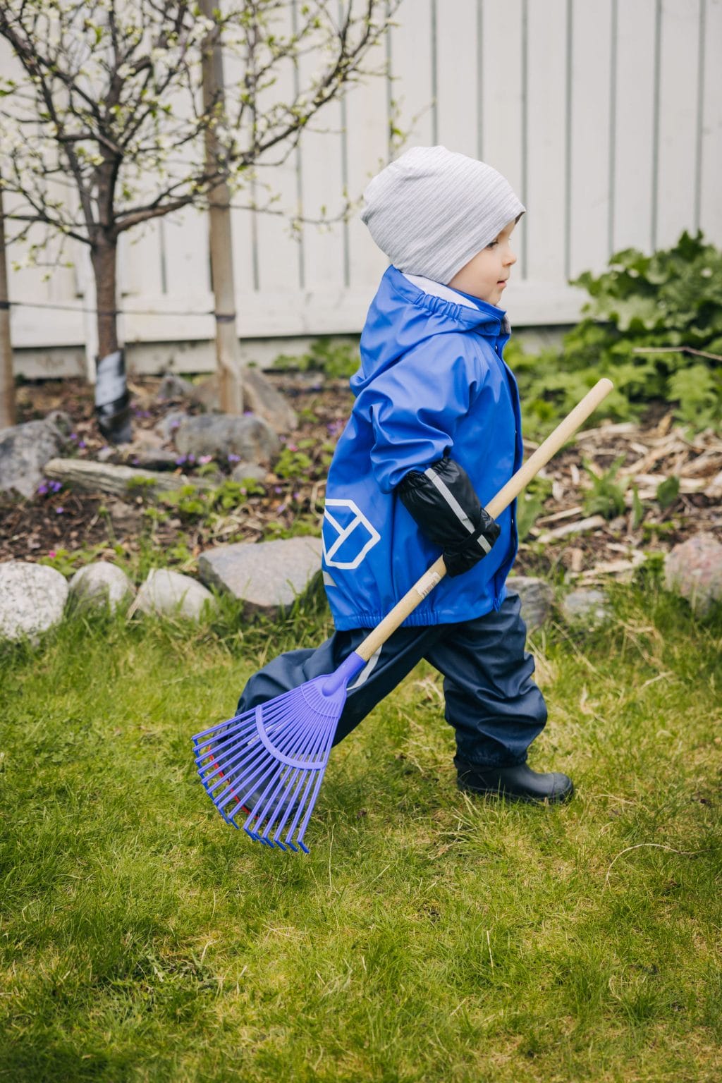 Lapsi kävelee puutarhassa pienen haravan kanssa.