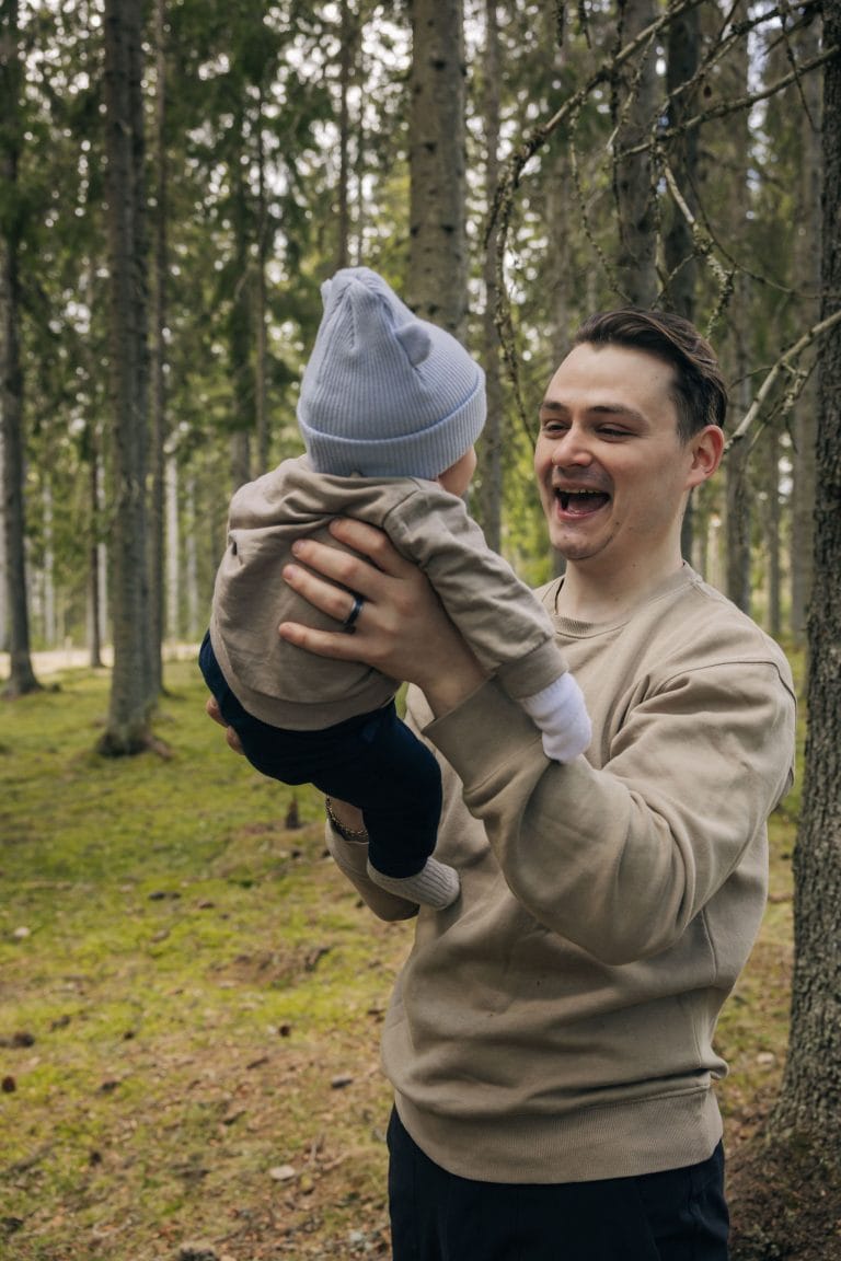 Vauva on isän sylissä metsässä ja isä hymyilee vauvalle.