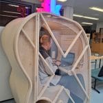 Kaarevamuotoinen 3D-tulostettu hiljainen tila, jossa ihminen istuu ja kannattavan tietokoneen äärellä.
