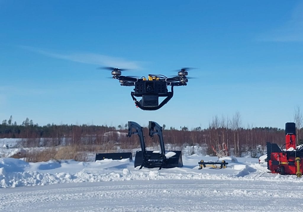 Nelilapainen drooni ilmassa kirkkaana talvipäivänä peltoaukealla.