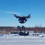 Nelilapainen drooni ilmassa kirkkaana talvipäivänä peltoaukealla.