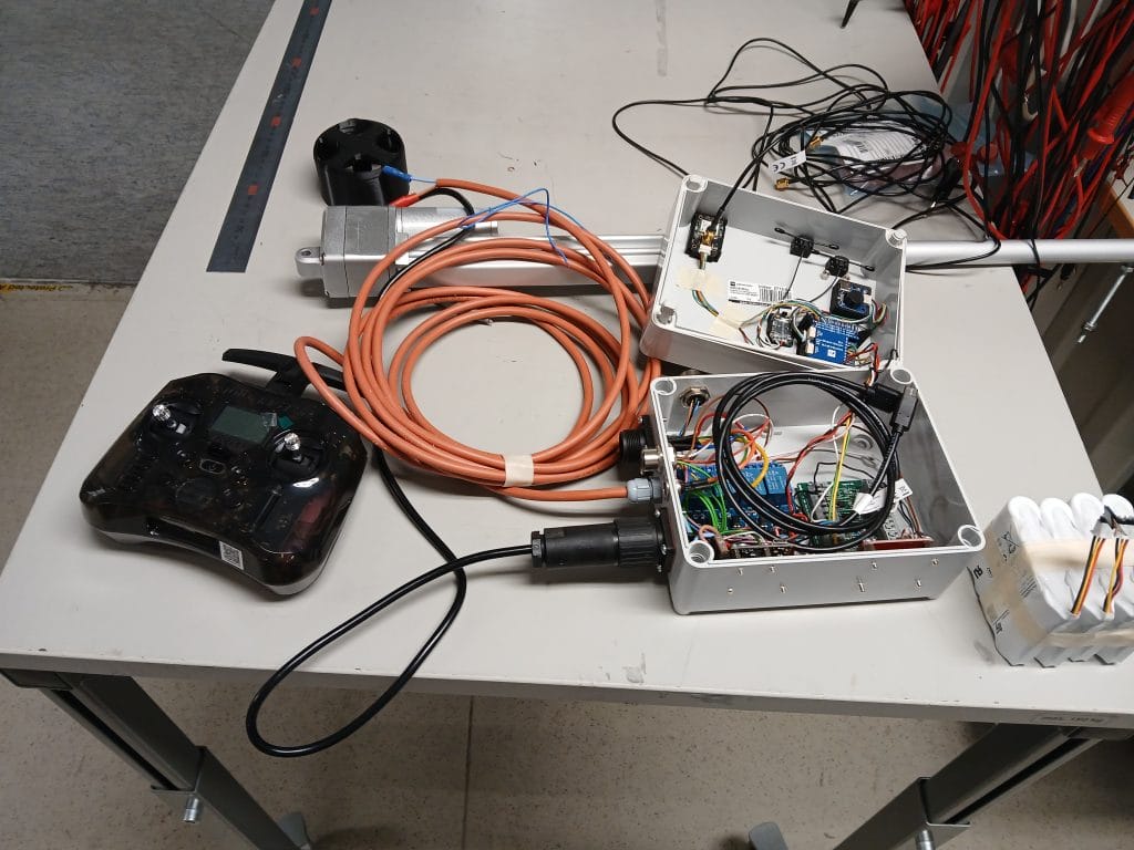 Työpöydällä auki oleva muovikotelo, jossa elektroniikkaa. Kotelosta lähtee kaapelit työntötangolle ja sähkönsyötölle.