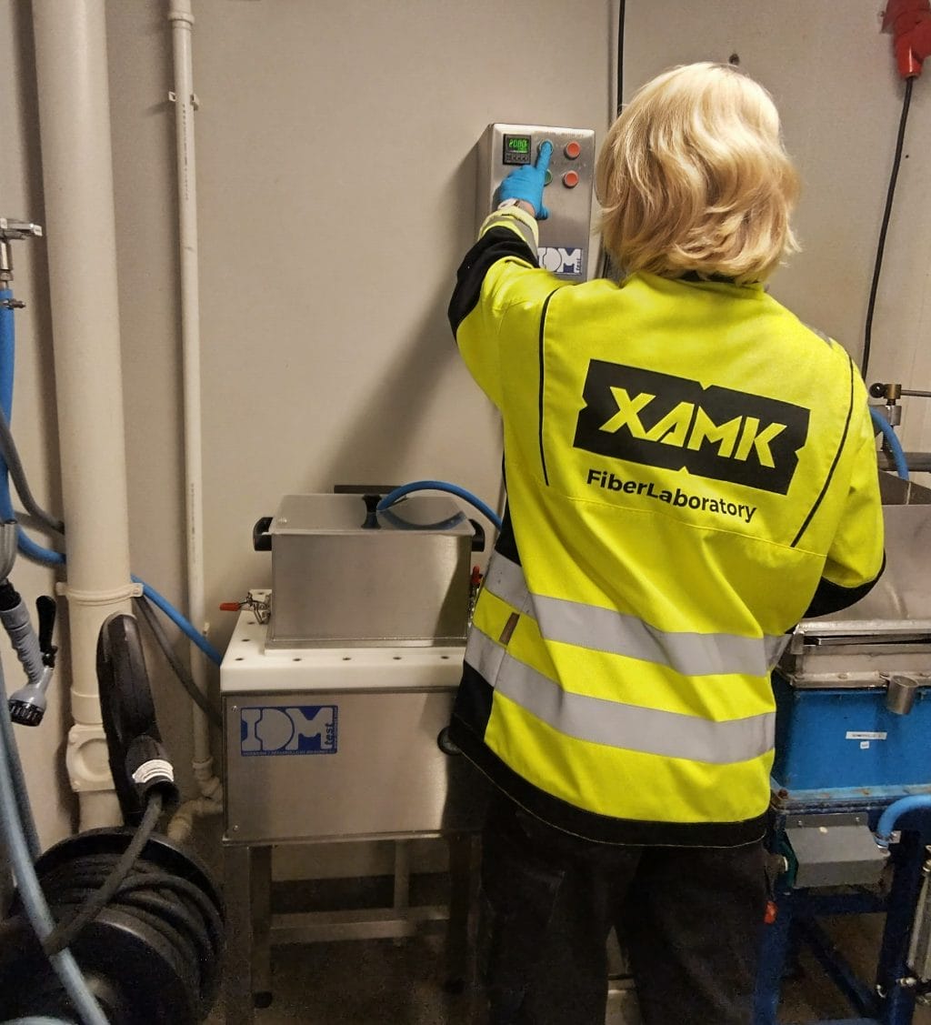 Ihminen keltaisessa liivissä painelemassa laitteen nappeja kuitulaboratoriossa.